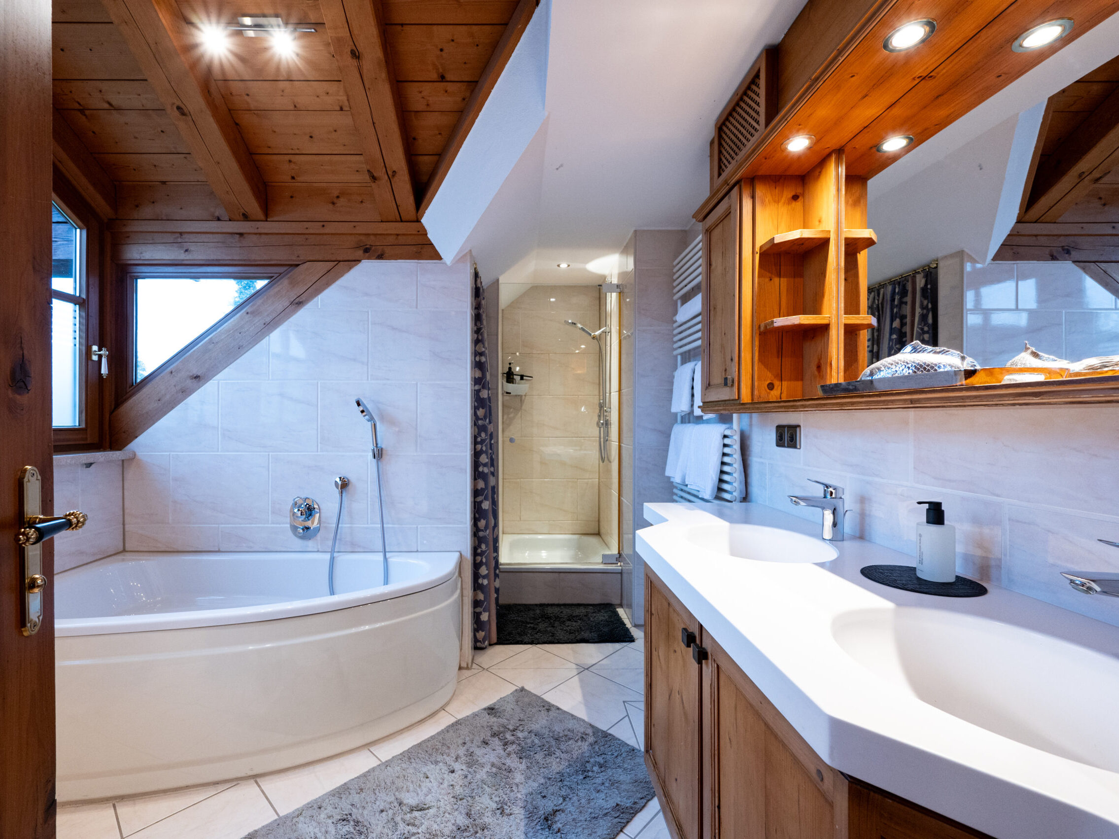 Badezimmer mit Eckbadewanne, Doppelwaschbecken, Dusche und Holzdetails.