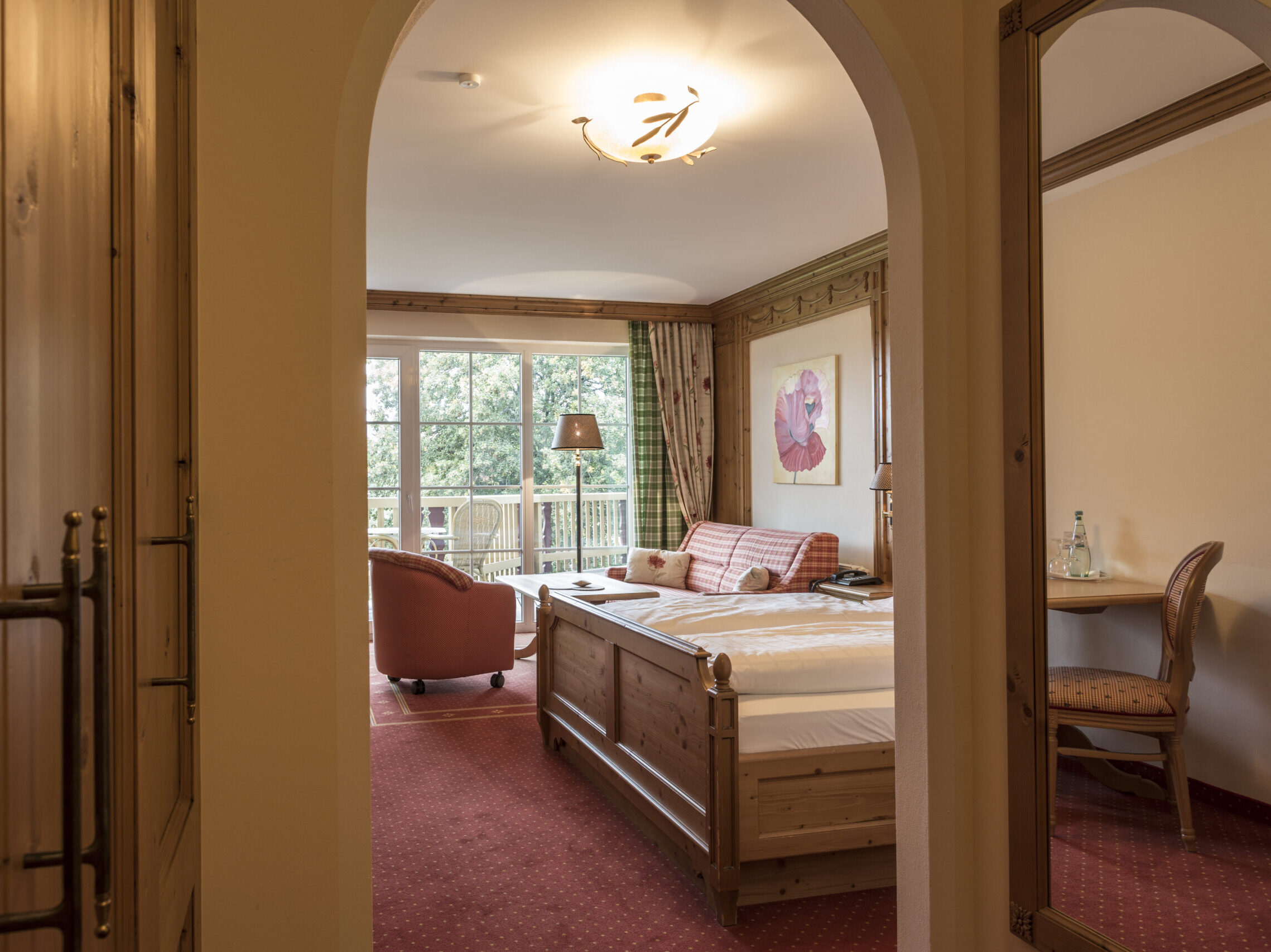Zimmeransicht des Comfort Zimmer mit Balkon im Landhausstildurch einen Rundbogen mit Blick auf Bett, Sitzgruppe und Balkon im Meiser SPA Resort