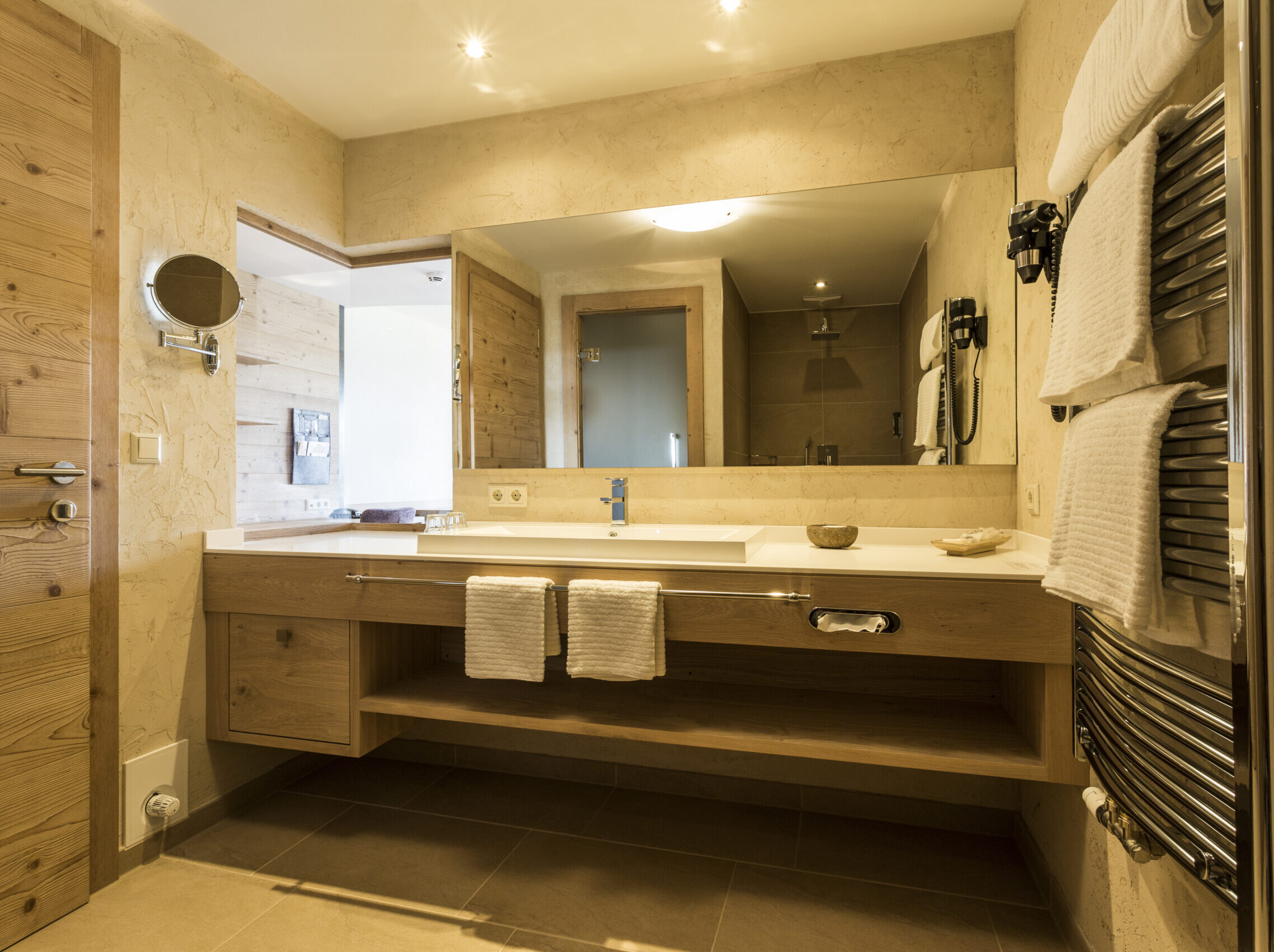 Junior Suite Superior mit Balkon im Meiser SPA Resort. Mit Blick ins Badezimmer, XXL Regendusche, großer Spiegel und elegantem Holzdesign